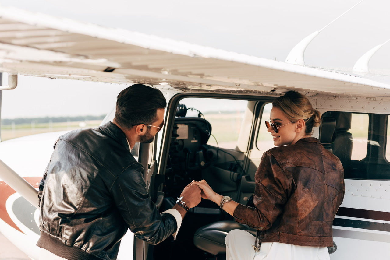 man supports a woman's hand romantically while she steps in a small fixed wing aircraft